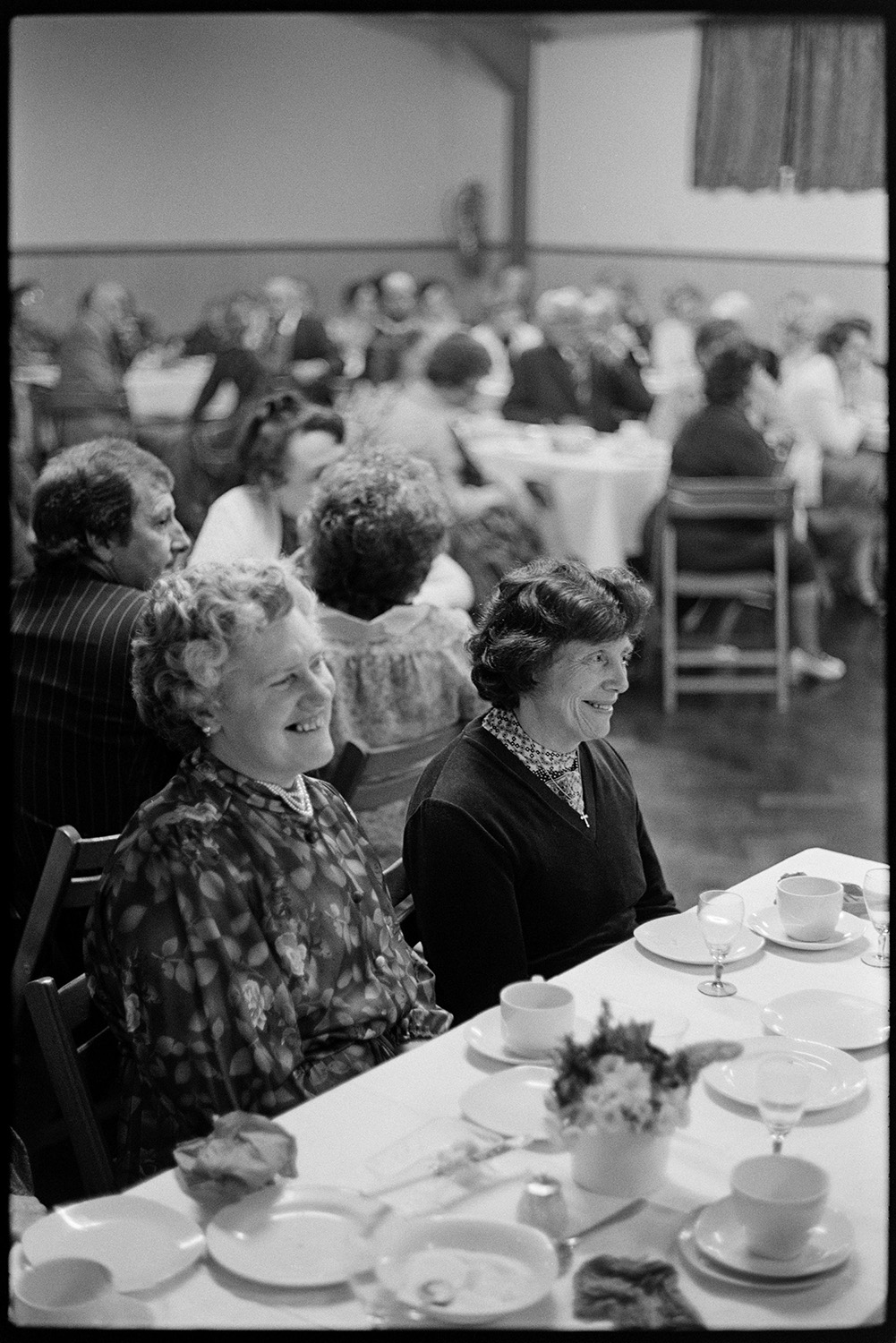 W I Centenary dinner, woman cutting cake, entertainment play on stage. 
[Women sat at tables at the Women's Institute Centenary Dinner in Dolton Village Hall.]