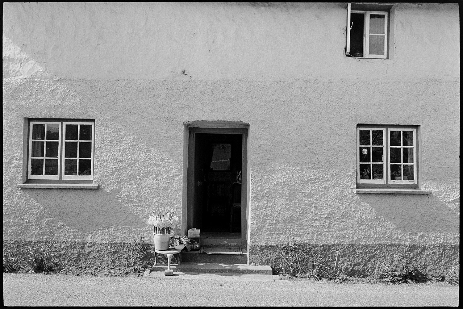 Woman putting flowers for sale at roadside in front cottage. Nice windows. 
[Flowers for sale outside a cottage near Umberleigh. The windows of the cottage are painted.]