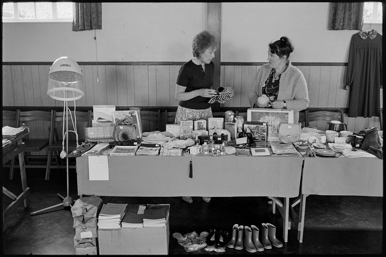 Schoolchildren giving concert in village hall, headmistress and children singing. 
[Two women running a bric-a-brac stall in an event at Dolton Village Hall. Various items are visible including books, wellington boots for children and a hairdryer.]