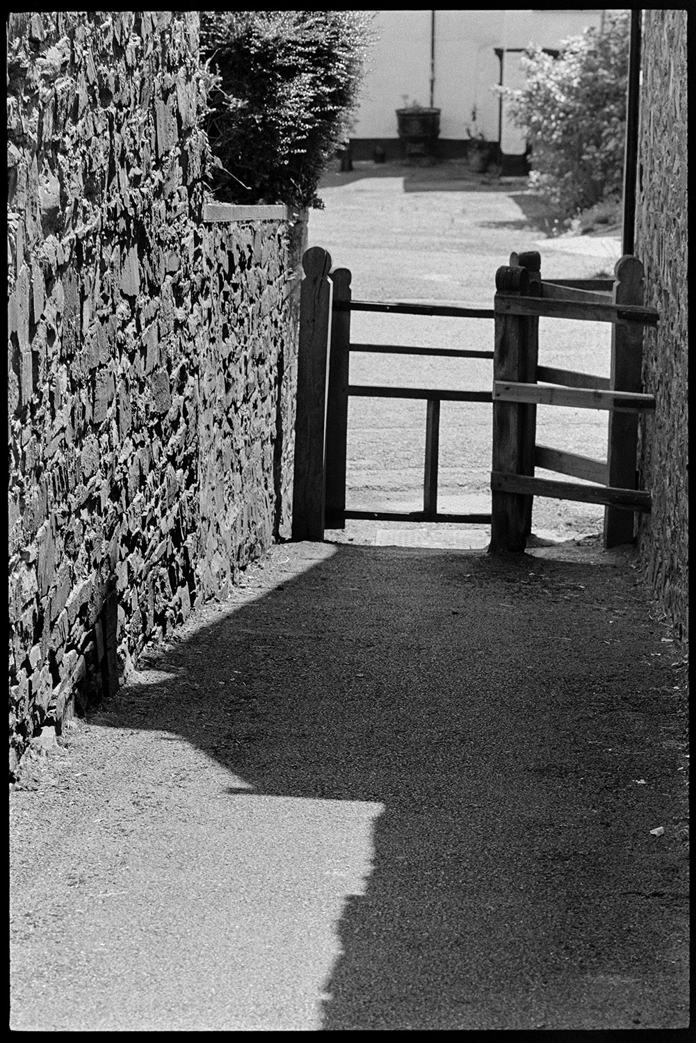 A walled footpath leading to a kissing gate, possibly in Dolton. The shadow of a building is falling across the path. James Ravilious took this image as a test shot to experiment with a new lens.