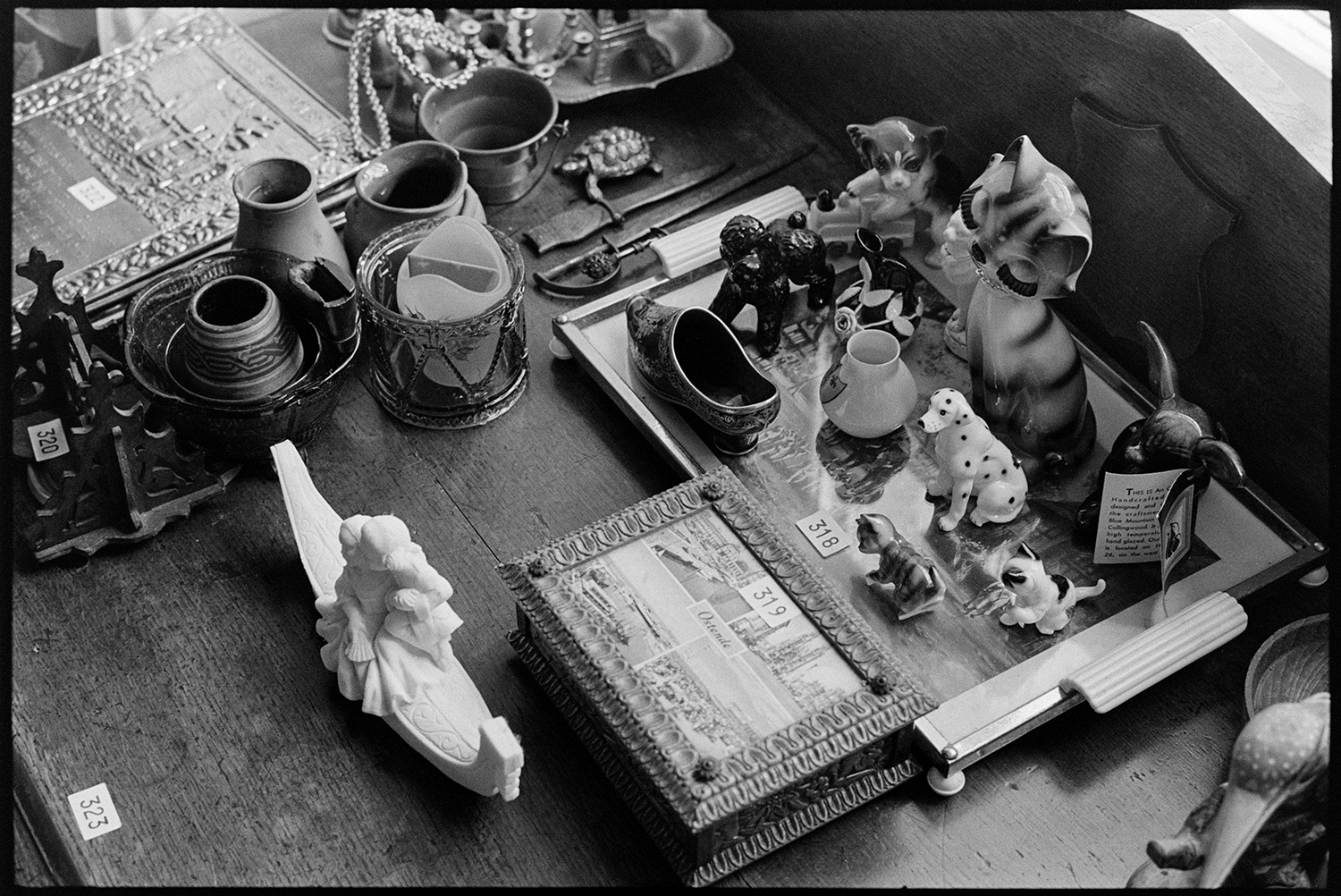 China, clocks and ornaments on viewing day, before house sale fireplace, painting. 
[China ornaments, pots, letter openers and a decorated box displayed on a desk at Arscotts House, Dolton, on the viewing day before the contents of the house are sold.]