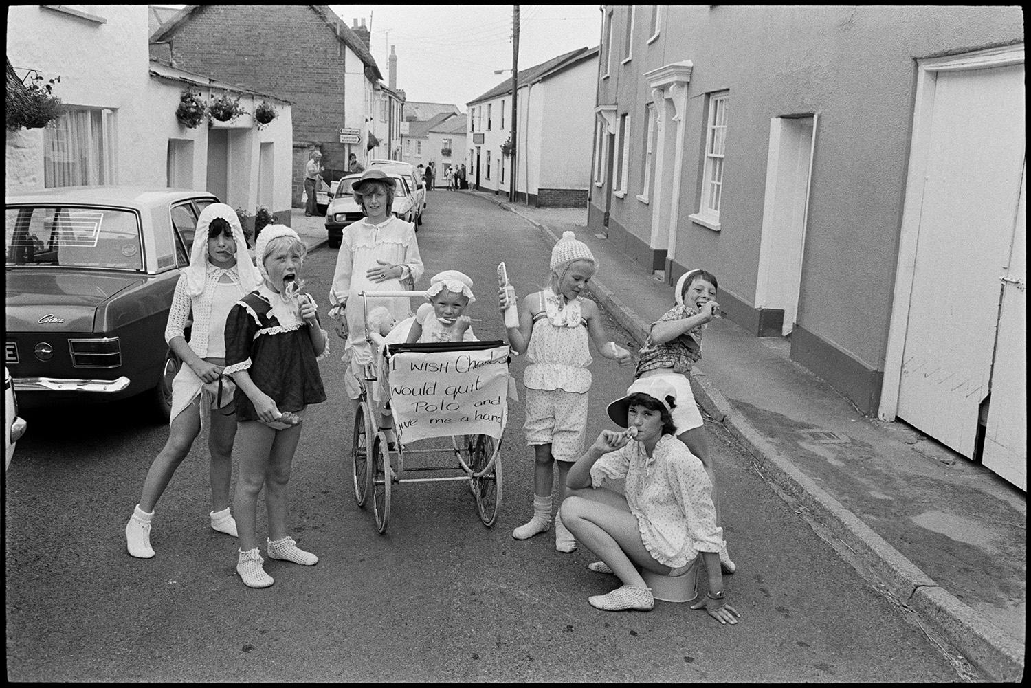 Fancy dress parade with brass band, going home afterwards. 
[Children in fancy dress as Diana Princess of Wales and Prince William, with a pram, at Chulmleigh Fair. The sign on the pram reads 'I wish Charles would quit Polo and give me a hand'. One child is sat in the pram and some of them are eating ice creams.]