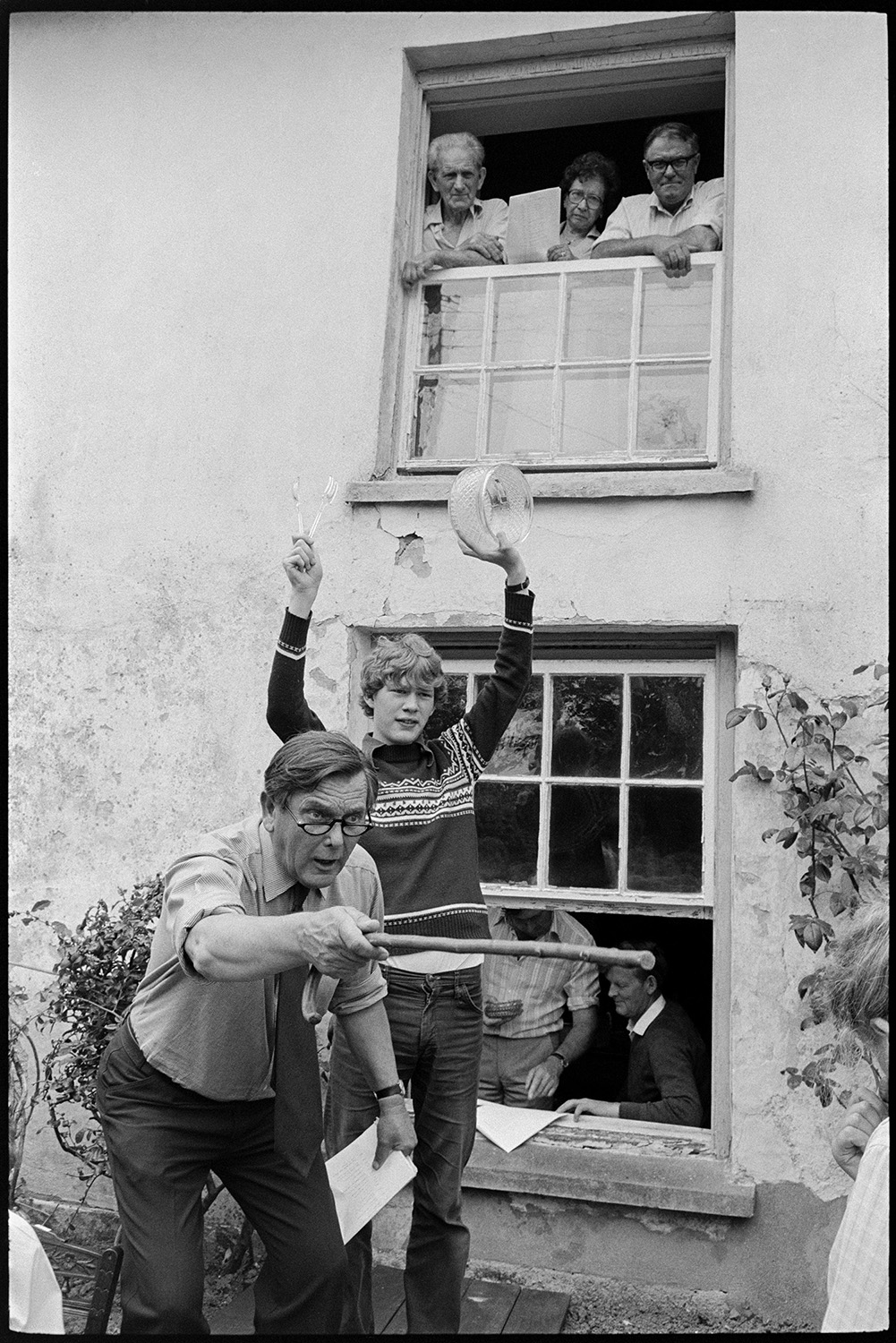 Auction of house contents, crowd, auctioneer and wife acting as clerk. 
[Paul Foggo auctioning the contents of Arscotts House in Dolton. He is using a walking stick to point to bidders and a boy is holding up the items for sale behind him. People are watching the auction from the windows of the house.]
