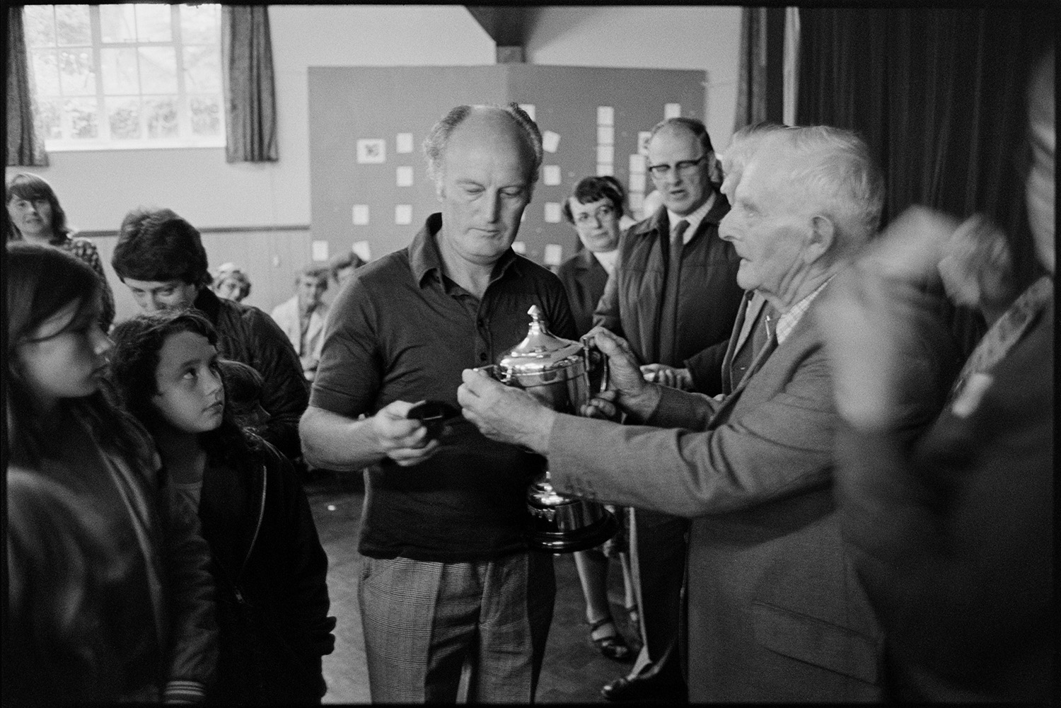 Cup winners after flower show. 
[Michael Mitchell being presented with a silver cup for his entry in the Dolton Flower Show at Dolton Village Hall. Children, Men and women are watching him.]
