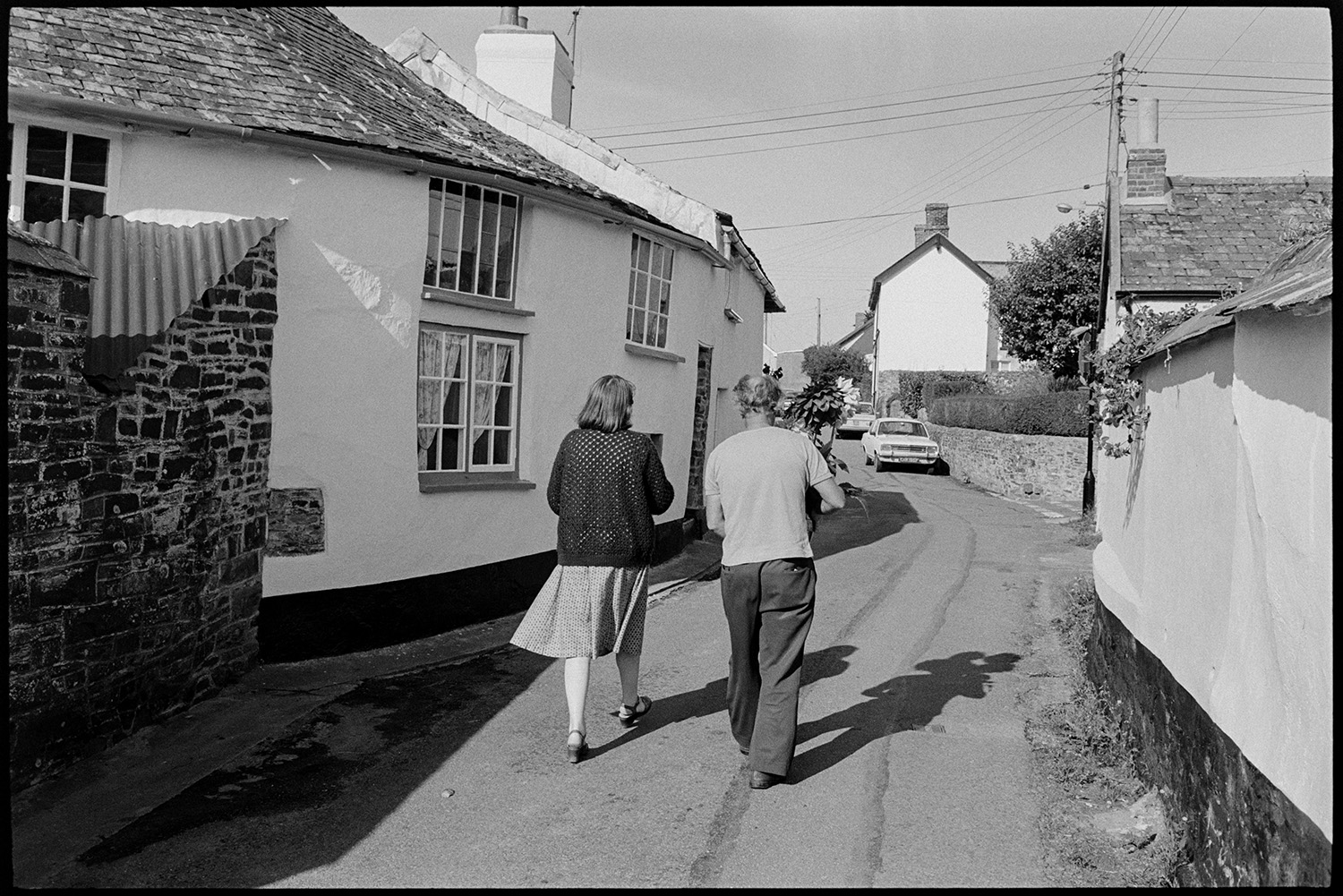 Preparing vegetables and flowers, flower show, boot of car with vegetables, chrysanthemums. 
[Rose Mitchell and Michael Mitchell, carrying a vase of Dahlias, along Aller Road in Dolton on their way to Dolton Flower Show. They are passing cottages.]
