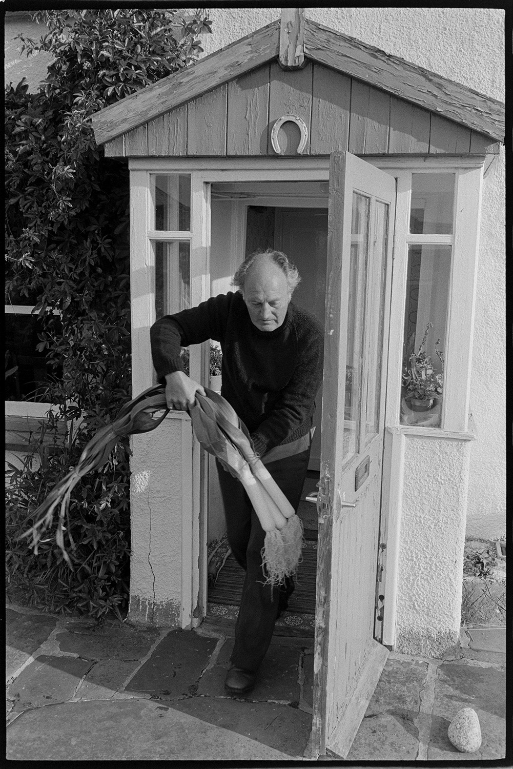 Preparing vegetables and flowers, flower show, boot of car with vegetables, chrysanthemums. 
[Michael Mitchell carrying leeks outs through the porch of Pear Tree Cottage, Aller Road, Dolton, to take to Dolton Flower Show. A horseshoe is hung above the porch door.]