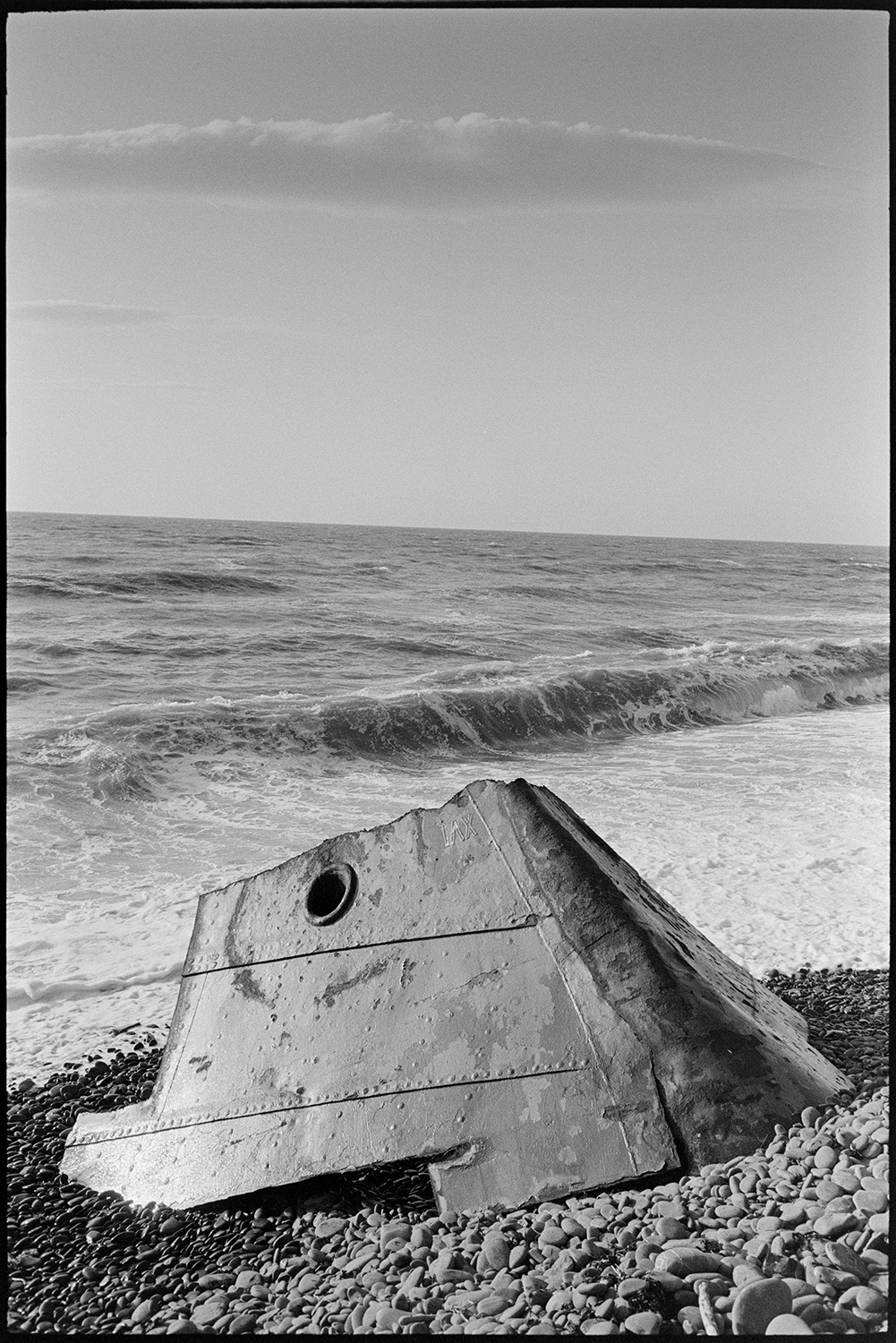 Evening seascape with section of wrecked boat on pebble beach. 
[Part of a wrecked boat on the pebble beach by the shoreline at Bideford.]