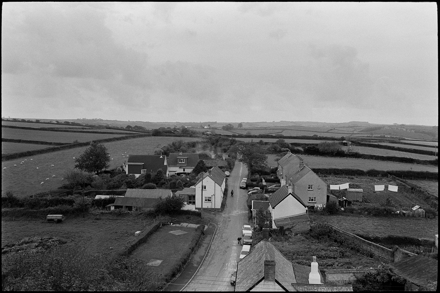 View from church tower. 
[A view of houses, a road and surrounding fields at Atherington, taken from Atherington Church tower.]