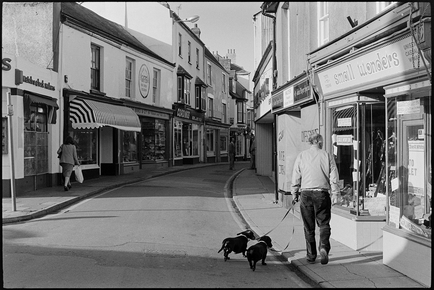 Street scenes with shop fronts, window display of clothes shop. 
[A man walking along Mill Street, Bideford with two dogs. He is passing 'Small Wonders' toyshop. Other shop front s are visible, including Cordings.]