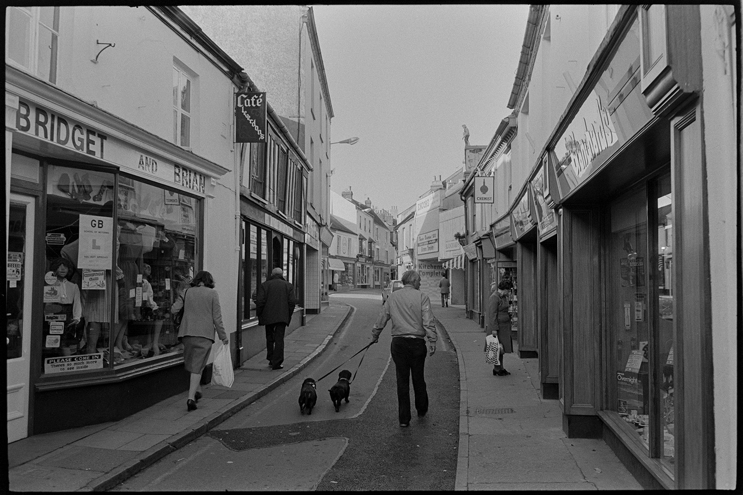 Street scenes with shop fronts, window display of clothes shop. 
[A man walking along Mill Street, Bideford with two dogs. Various shop front can be seen including 'Bridget and Brian' and 'Café Cleverdons'. Other shoppers are also walking along the street.]
