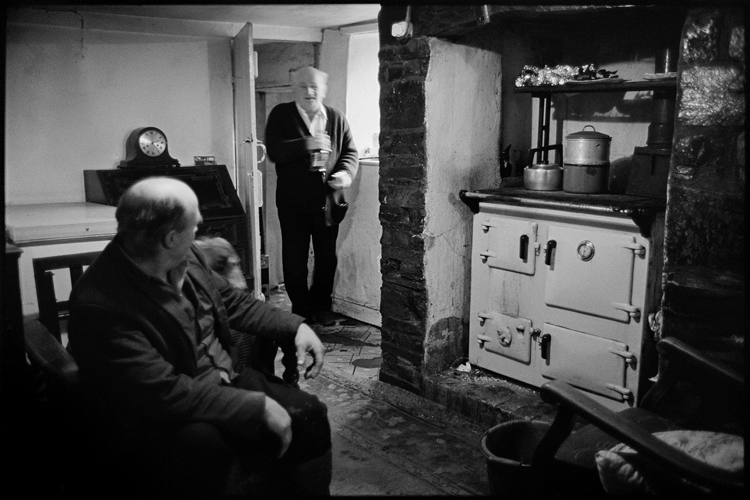 Waiting for Christmas dinner. Woman cooking turkey. Rayburn stove, carving turkey, eating. 
[Archie Parkhouse and another man in the kitchen by a Rayburn stove at Horseshoe Cottage on Christmas Day, before their Christmas dinner.]