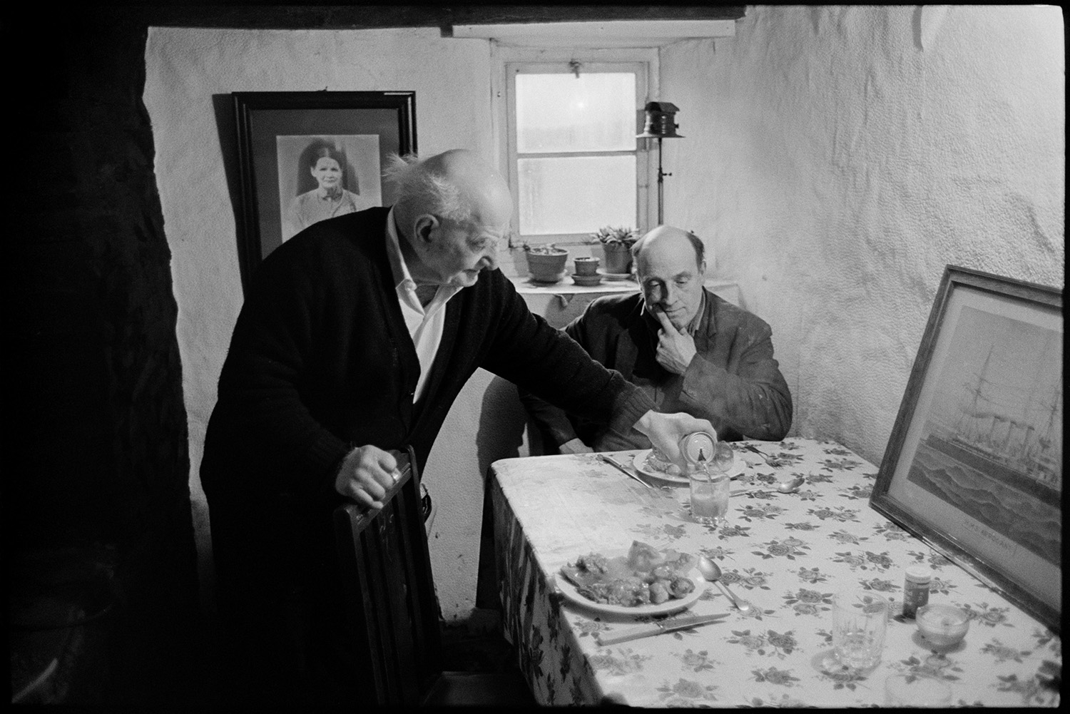 Waiting for Christmas dinner. Woman cooking turkey. Rayburn stove, carving turkey, eating. 
[Archie Parkhouse and another man sitting down to eat their roast turkey Christmas dinner at Horseshoe Cottage, Dolton on Christmas Day. Archie Parkhouse is pouring a drink and a picture of a ship is on the table.]