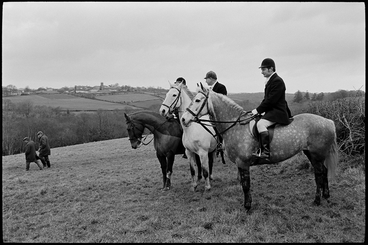 Hunt Meet, horses and followers setting off. 
[Three mounted huntsmen in a field at Highampton. Hunt followers can be seen behind them in the field.]