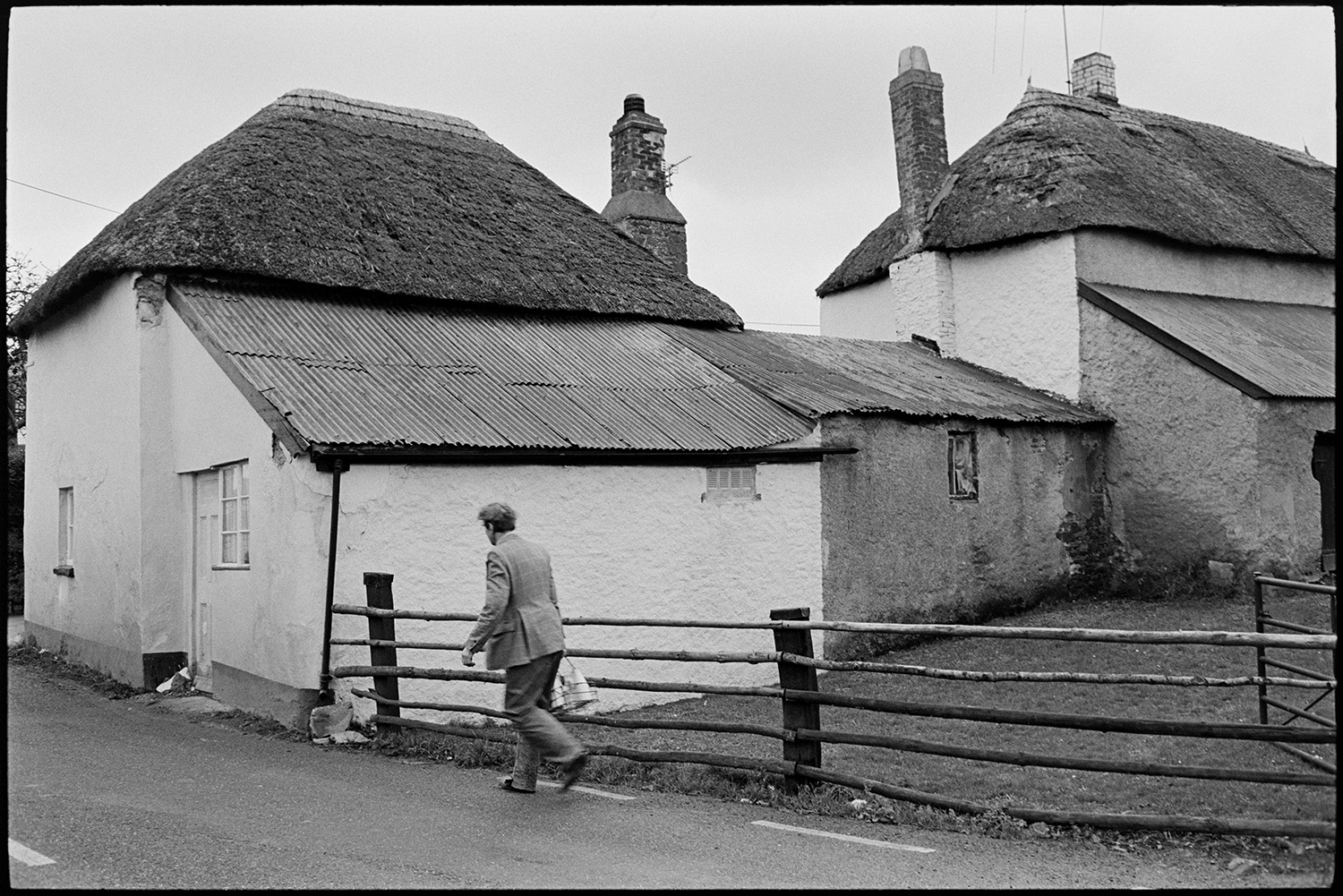 Farmer, milkman doing last milk round, showing new man the ropes, milk bottles.
[Ivor Bourne of Jeffrys farm delivering milk on his last milk round to Chaplands Cottage, Beaford. The cottage has a thatched roof with an extension with a corrugated iron roof.]