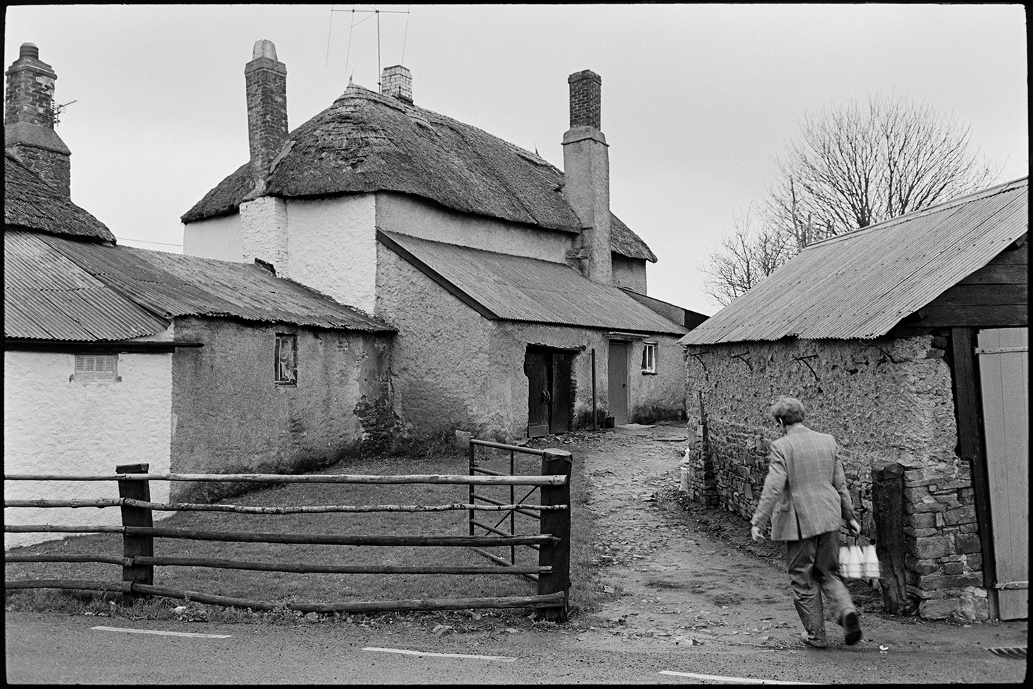 Farmer, milkman doing last milk round, showing new man the ropes, milk bottles.
[Ivor Bourne of Jeffrys Farm delivering milk on his last milk round to Chaplands, Beaford. The cottage is thatched and has an extension with a corrugated iron roof.]