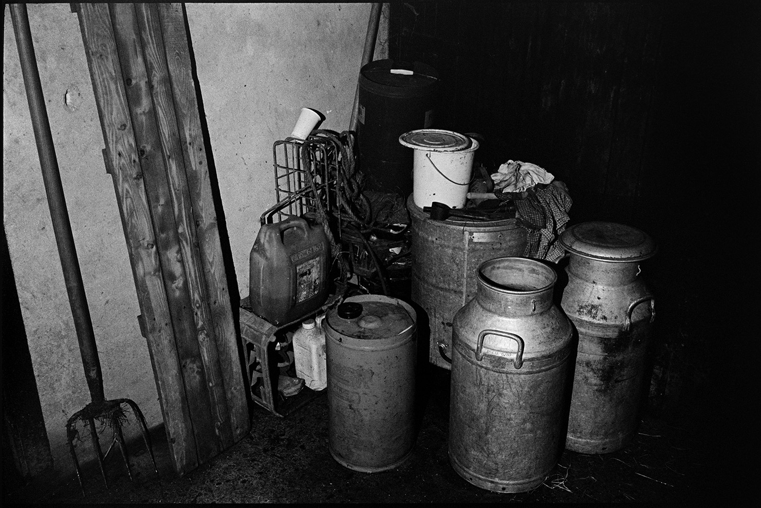 Milk churns, a fork and plastic contained amongst other items stored in a shed or barn at Jeffrys Farm, Beaford.