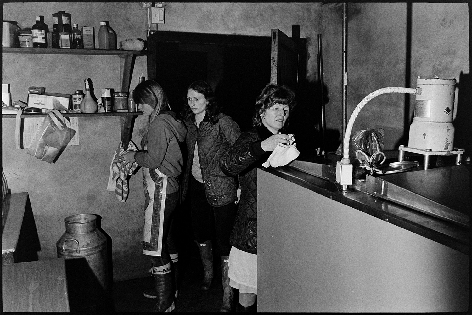 Women in dairy filling milk bottles, early morning.
[Three women, one of which is possibly Marylyn Bourne, working in the dairy at Jeffrys Farm, Beaford in the early morning. The farm was also known as Mill Road Farm. A milk churn and various bottles are visible in the dairy.]