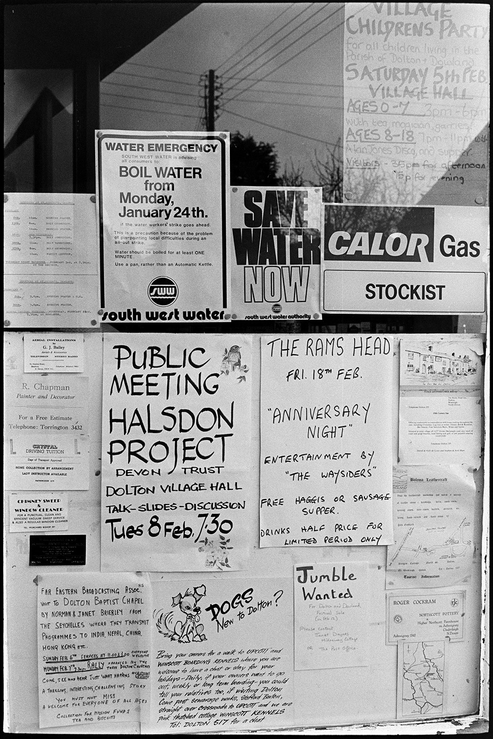 Posters, notices in Post Office window, events and meetings. <br />
[Notices in Beaford Post Office Window. Adverts for a Children's Party in the village hall, an Anniversary Night at The Rams Head pub, a meeting about the Halsdon Project and a notice from South West Water, are displayed amongst other adverts.]