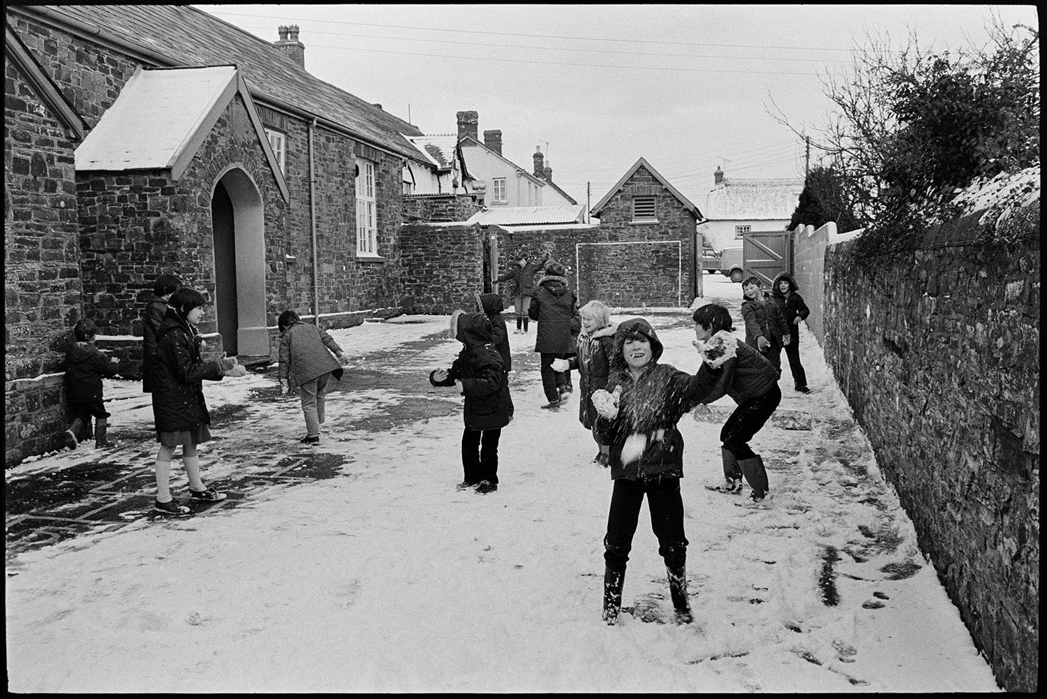 Snow, children throwing snowballs in school playground. 
[Children having a snowball fight in Dolton Primary School playground. A child in the foreground is throwing a snowball at the camera.]