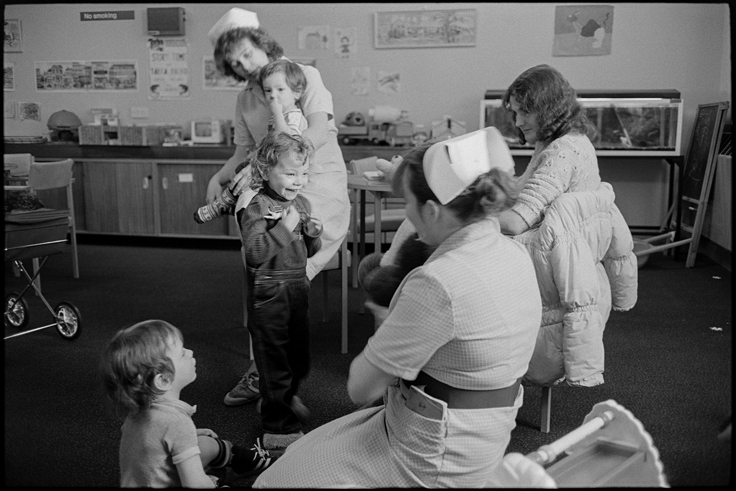 Hospital children's ward, nurses, mothers with children in wards, Sister at ward, cuddly toys. 
[Two nurses and a woman playing with children in a room on the Children's Ward at Barnstaple General Hospital. Toys and posters are visible in the room.]