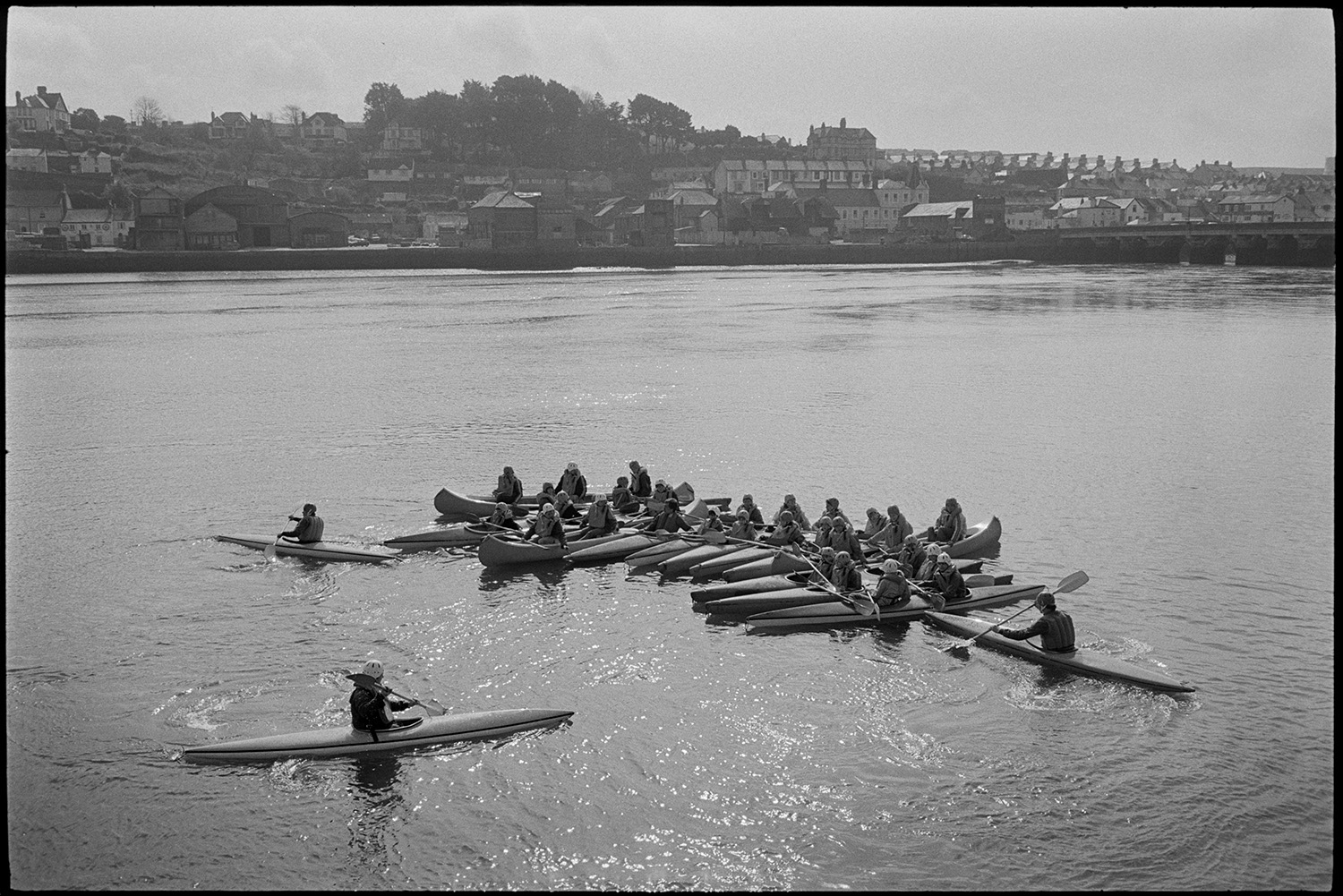 Canoeists on river, quayside capsized canoe! Houses on waterfront. <br />
[People having a canoeing lesson on the River Torridge by Bideford Long Bridge, also known as Bideford Old Bridge. Houses can be seen along the waterfront in the background.]