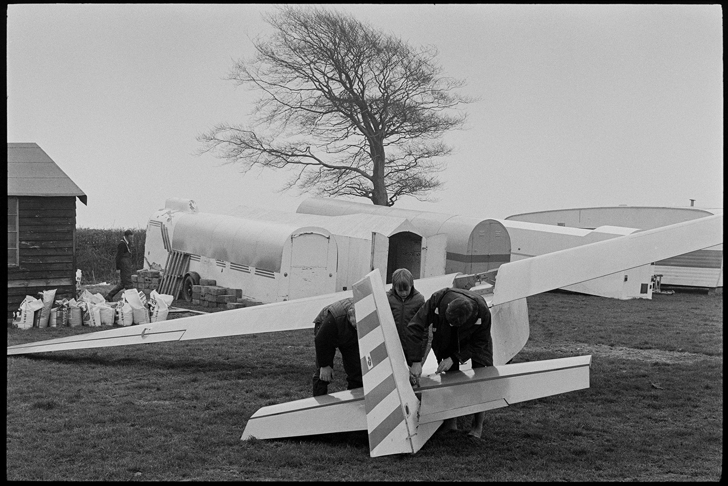 Glider at flying club. 
[Two men and a boy looking at a glider at a flying club at Eaglescott, Burrington. Trailers on wheels can be seen in the background.]