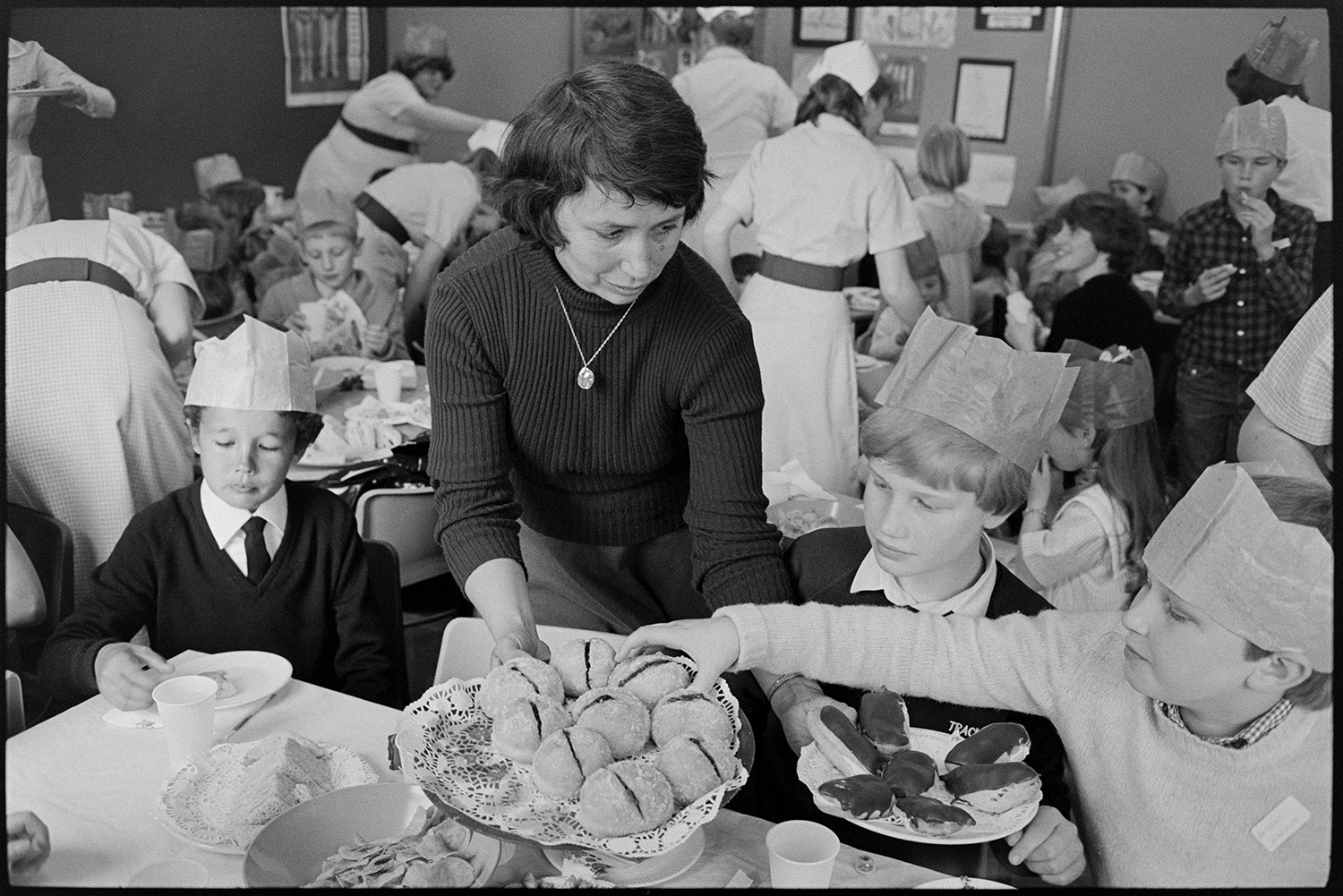 Party in children's ward of Hospital, food and drink served by nurses, buns, cakes. <br />
[A woman serving cakes to three boys at a party on the Children's ward at Barnstaple General Hospital. Other children can be seen in the background and some of them are wearing paper hats.]