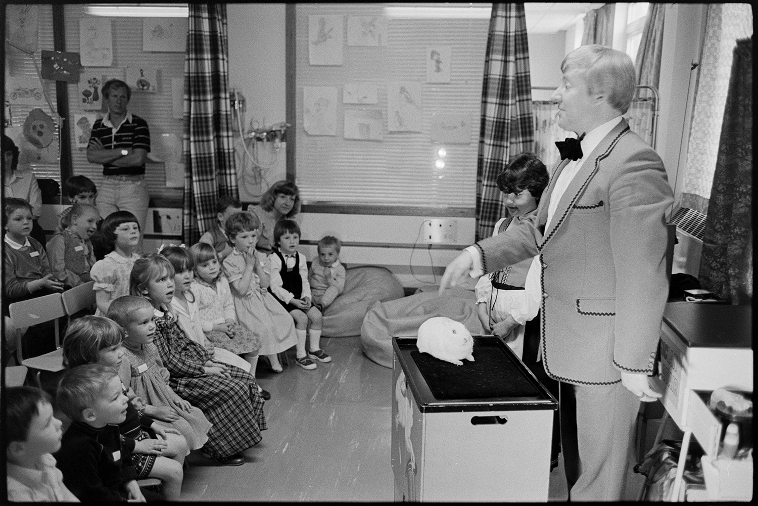 Conjuror at children's party in hospital. <br />
[Ian Adair, a magician, entertaining children at a party on the Children's Ward at Barnstaple General Hospital. He has a rabbit in front of him.]