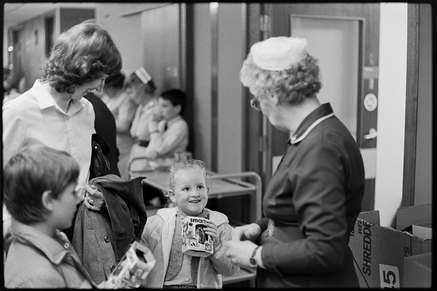 Ward Sister and nurses in ward of hospital. 
[The Ward Sister or Matron of the Children's Ward in Barnstaple General Hospital handing out Easter eggs to two children with a woman.]
