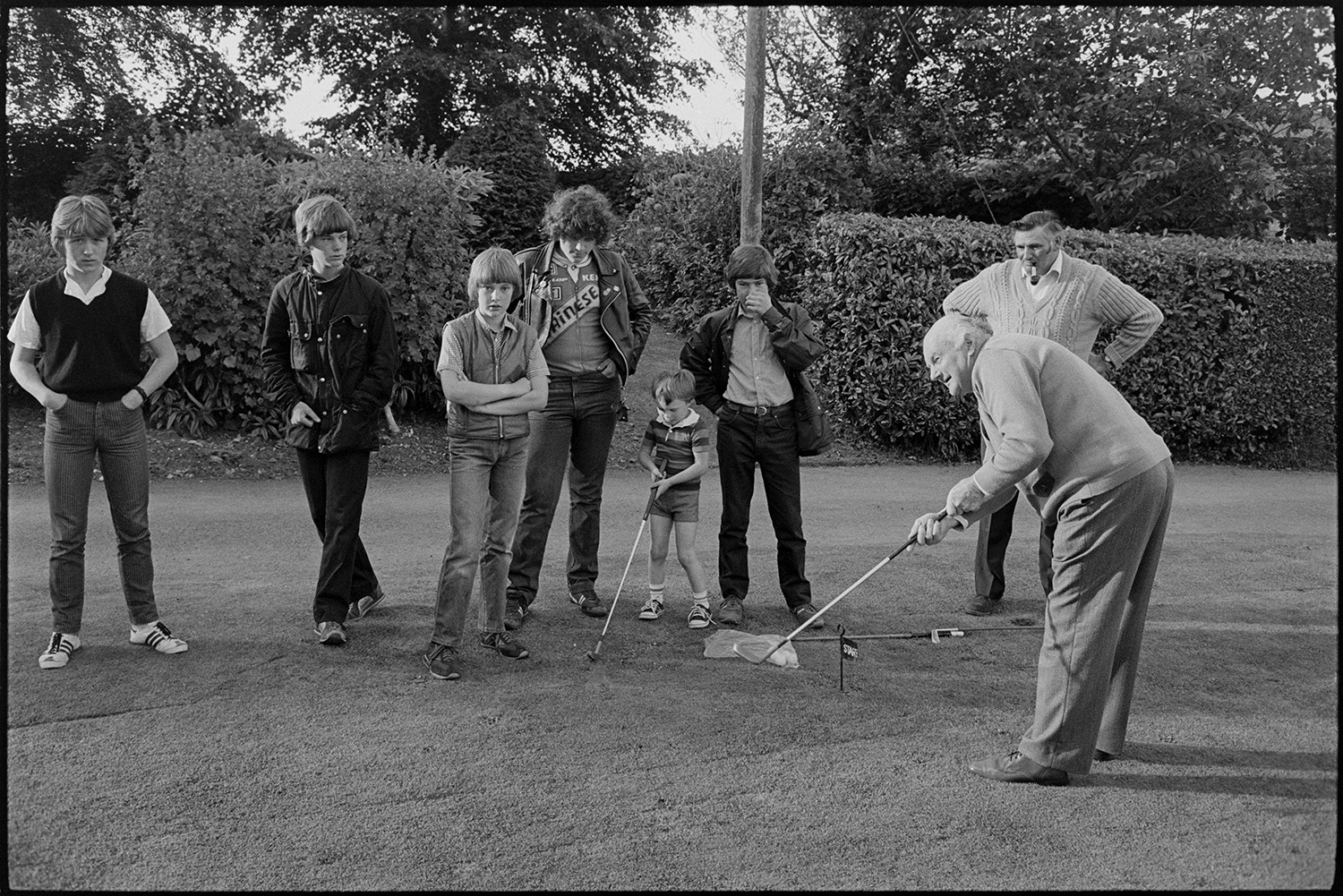 Sideshows at garden fete, bowls, hoop la, billiards, golf.
[Two men playing golf on the lawn at a fete at the Old Rectory, Merton with a line of children and teenagers watching. One of the men is smoking a pipe.]