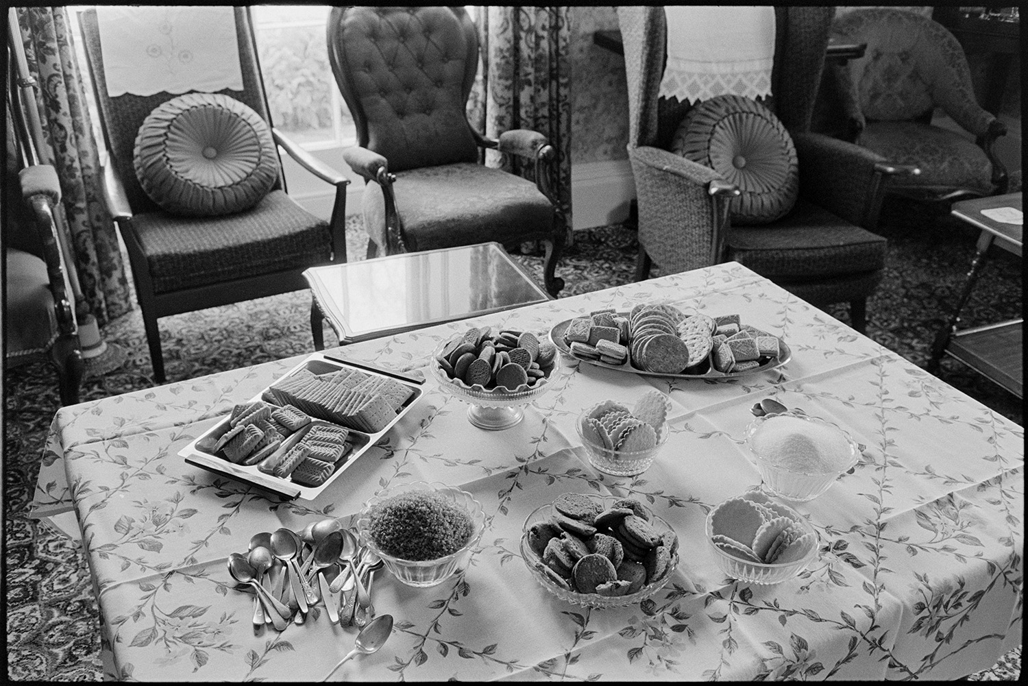 Biscuits laid out for tea at garden fete on table inside.
[Plates of biscuits laid out on a table in a room with armchairs at a fete at the Old Rectory, Merton.]