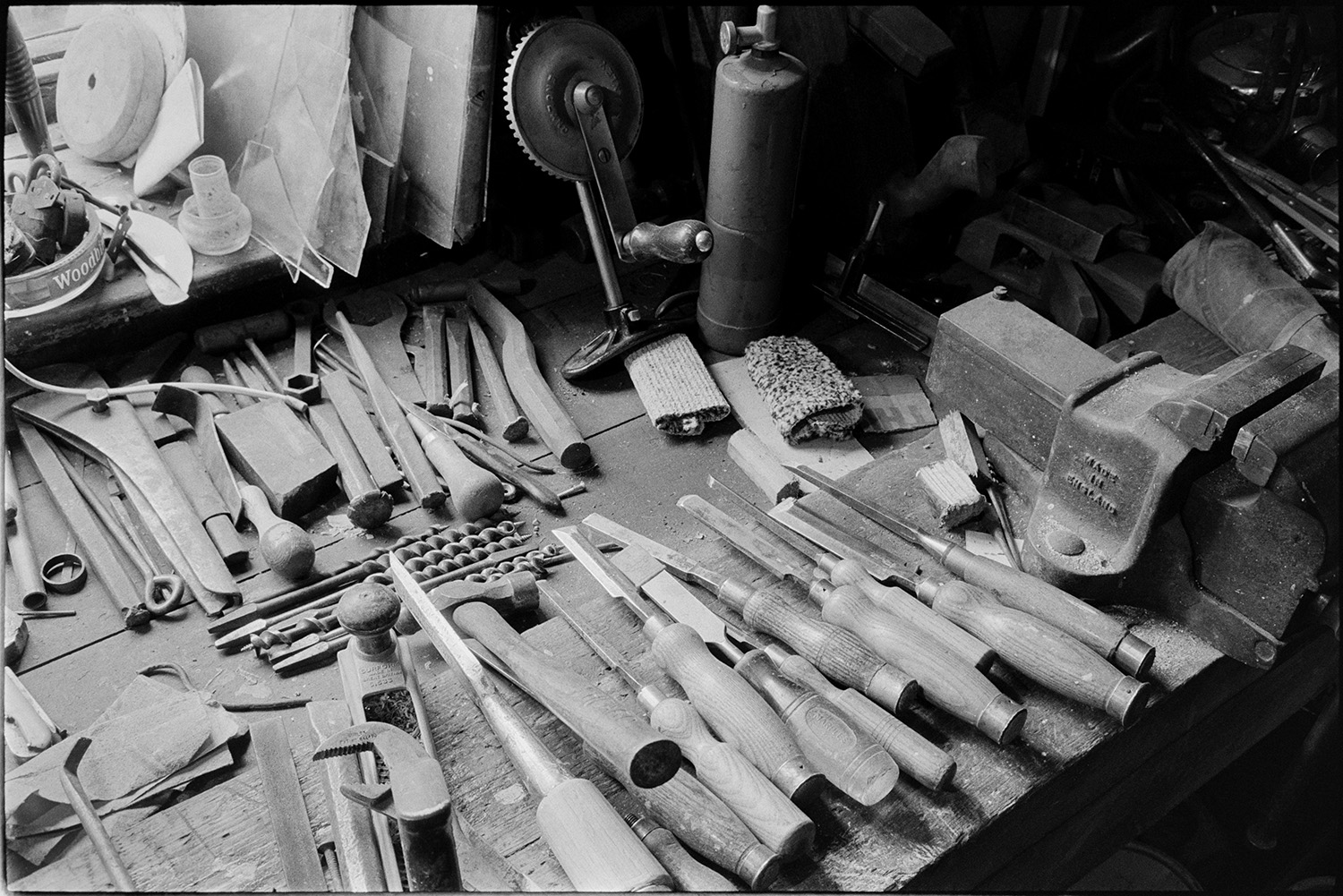 Tools, chisels etc on workshop bench. 
[Tools belonging to Bert Herd, including chisels, a hand drill and a vice on a workshop bench at Arscotts, Dolton.]