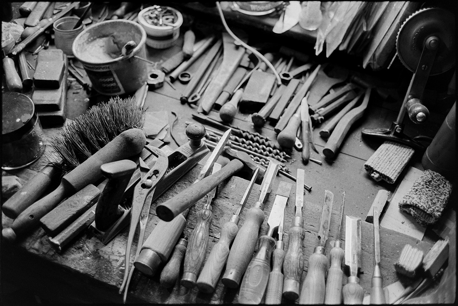 Tools, chisels etc on workshop bench. 
[Tools belonging to Bert Herd, including chisels, a brush, a hand drill and drill bits on a workshop bench at Arscotts, Dolton.]