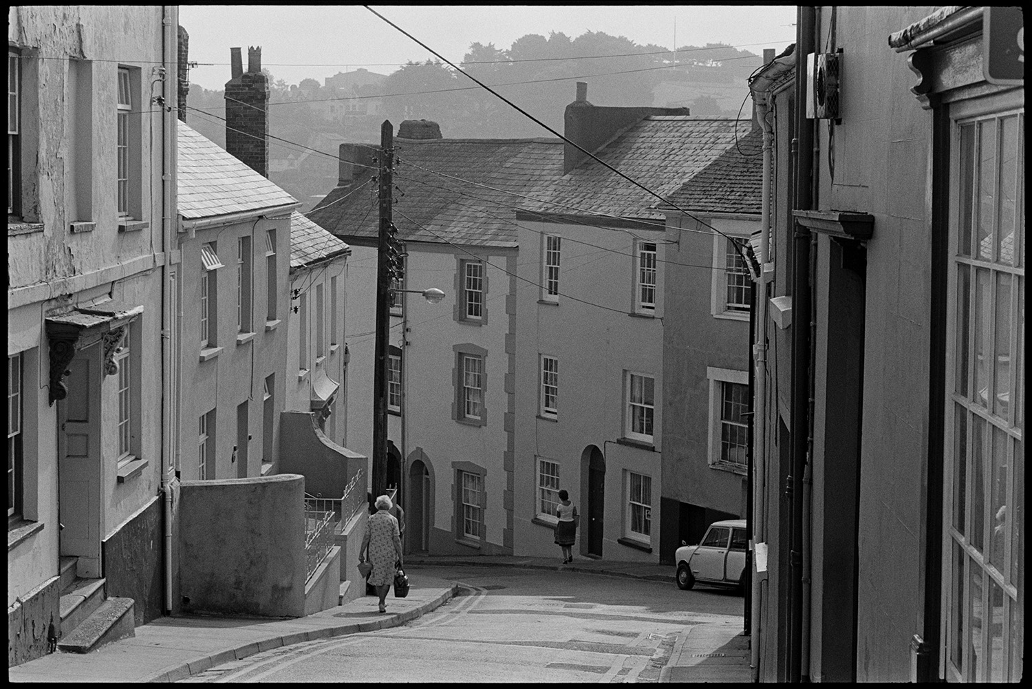 Street scenes, hill. 
[Two women walking past terraced houses down a hilly street in Bideford.]
