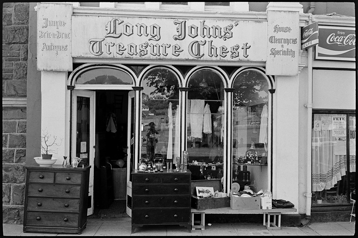 Interior of Antique shop, also exterior view of front of shop. 
[The shop front window of Long Johns' Treasure Chest antique shop on Bideford Quay. Various items including two chests of drawers are on display outside the shop.]