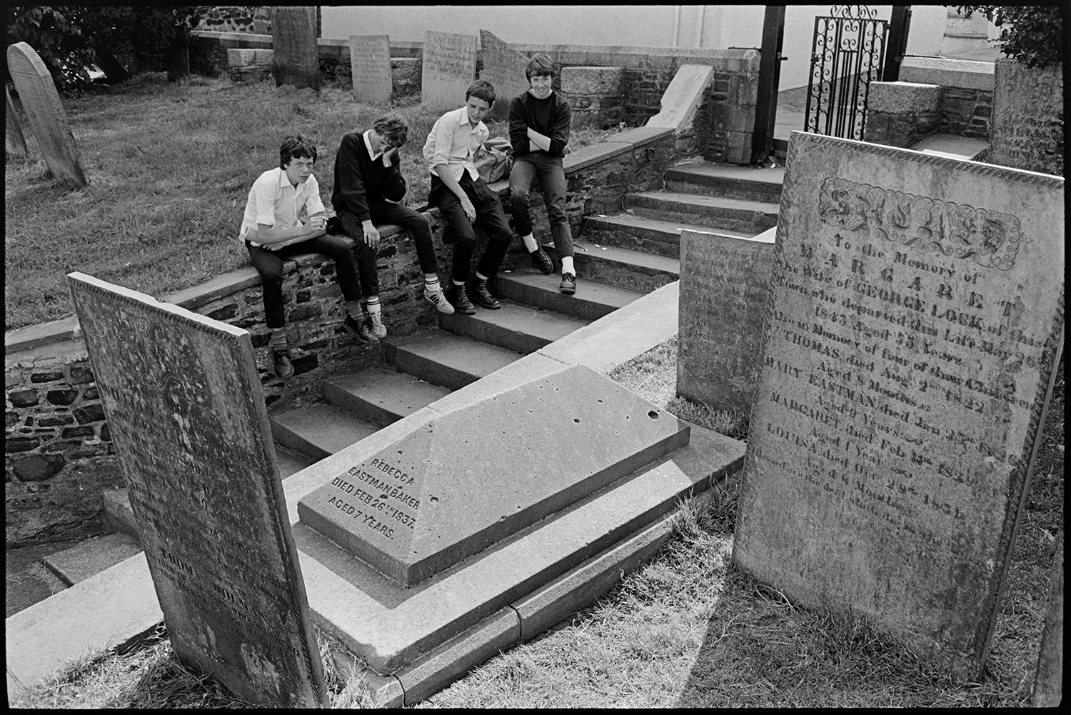 Street scenes, graveyard with boys sitting on wall. 
[Four boys sat on a wall by steps running through Bideford Churchyard. Gravestone can be seen in the foreground.]