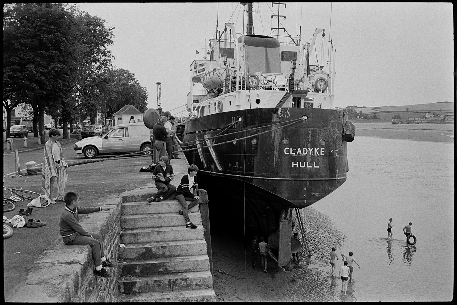 Children playing at quay with ship alongside quay, swimming. 
[Children playing by steps on Bideford Quay near to the Cladyke Hull which is moored alongside the Quay. Some children are swimming in the River Torridge near the ship.]