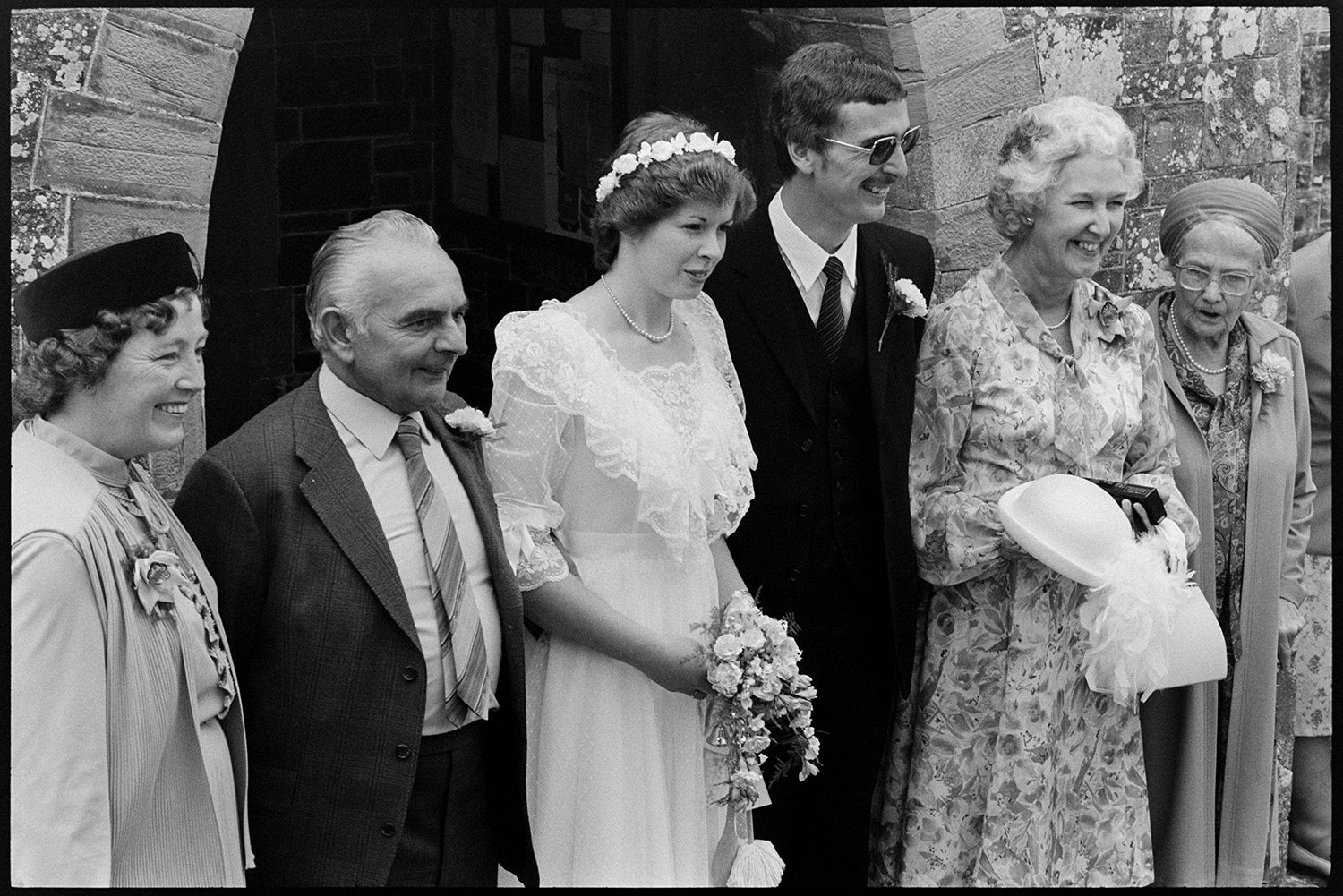 Wedding, groups, bride and groom leaving church, chatting to guests. 
[Cynthia Palmer, her groom and other wedding guests posing for a photograph outside the entrance to Dolton church after their wedding.]