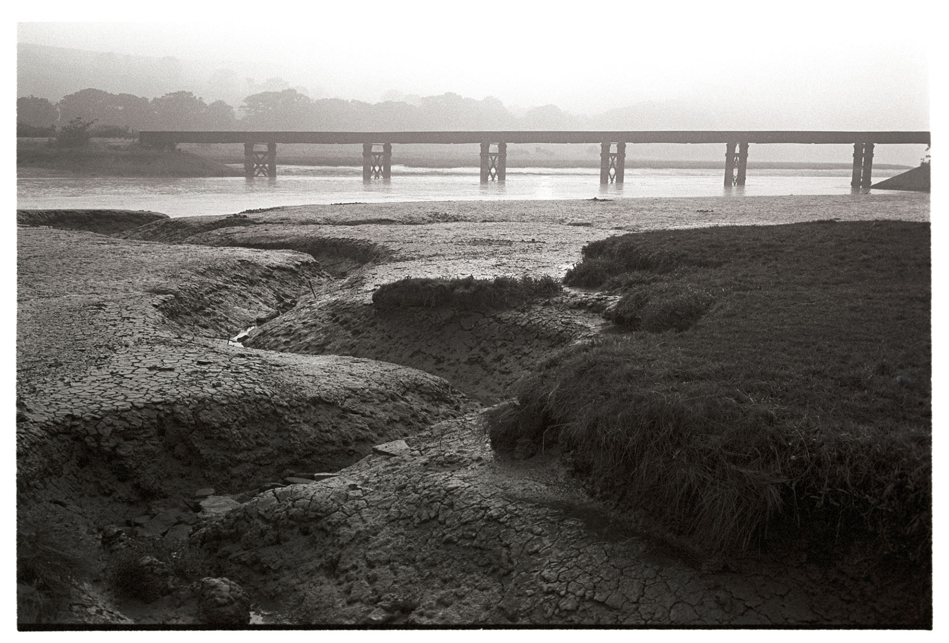 Sun rising over railway bridge over river, mudflats, low tide.
[The sun rising over the railway bridge across the River Torridge at Pillmouth, Landcross at low tide. Mudflats and the course of a rivulet are visible in the foreground.]