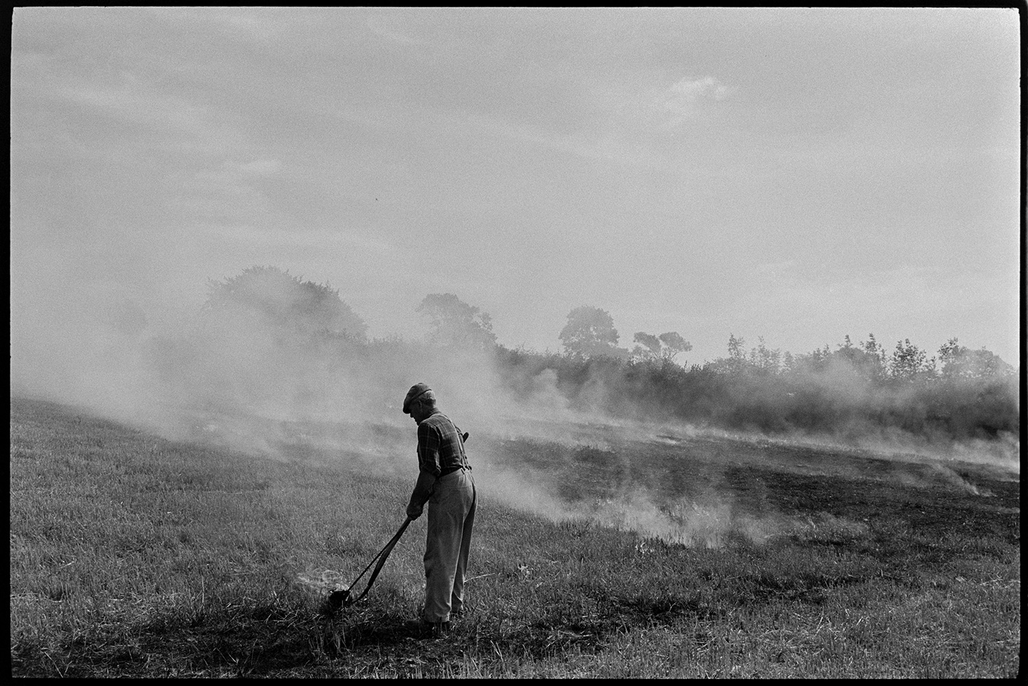 Farmer burning stubble. 
[Alf Pugsley burning stubble in a field at Lower Langham, Dolton. Smoke is rising from the field.]