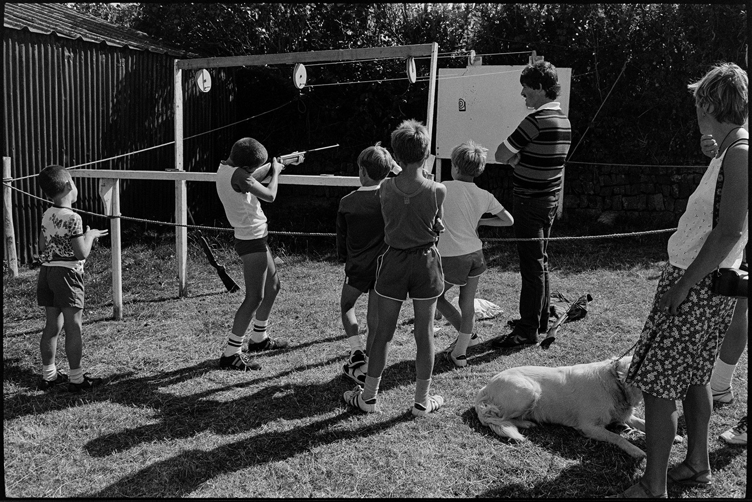 Fete, produce, stalls, machinery, flowers. 
[A group of boys playing a shooting game at a fete at either Monkleigh or Frithelstock. One boy is aiming his gun at the target.]