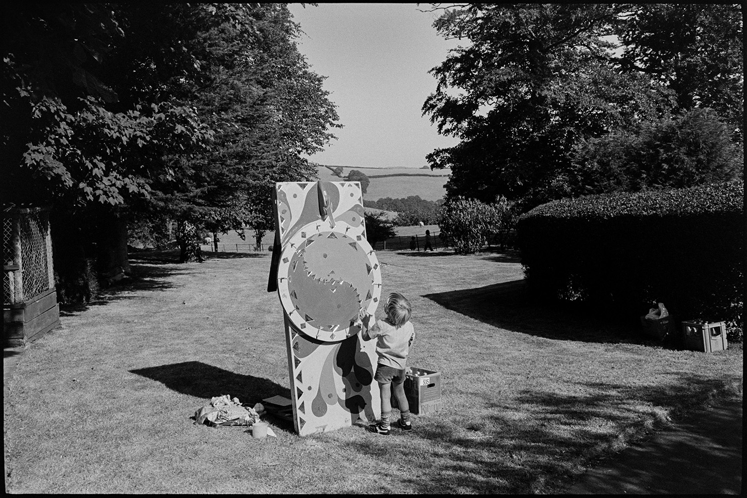 Blacksmith demonstrating at fete, wheel of fortune. 
[A child spinning a 'wheel of fortune' game in a field at a fete.]