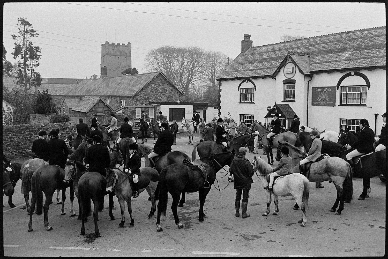 Hunt meet, horses and riders in village in front of pub. 
[Horse riders gathered for a hunt meet outside the Royal oak pub in Dolton. Dolton church tower can be seen in the background.]