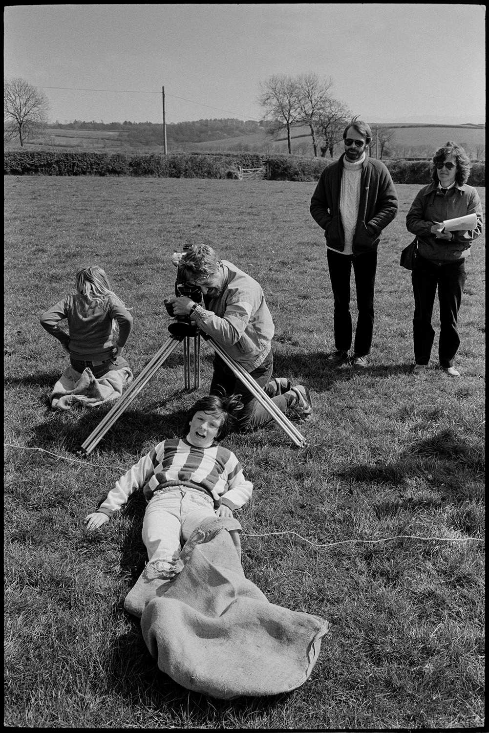 Club Day, sports, sack race, wellie throwing, man filming.
[Children being filmed by Malcolm Baldwin, using on a tripod, in a sack race in a field at Iddesleigh Club Day. Two people are watching in the background.]