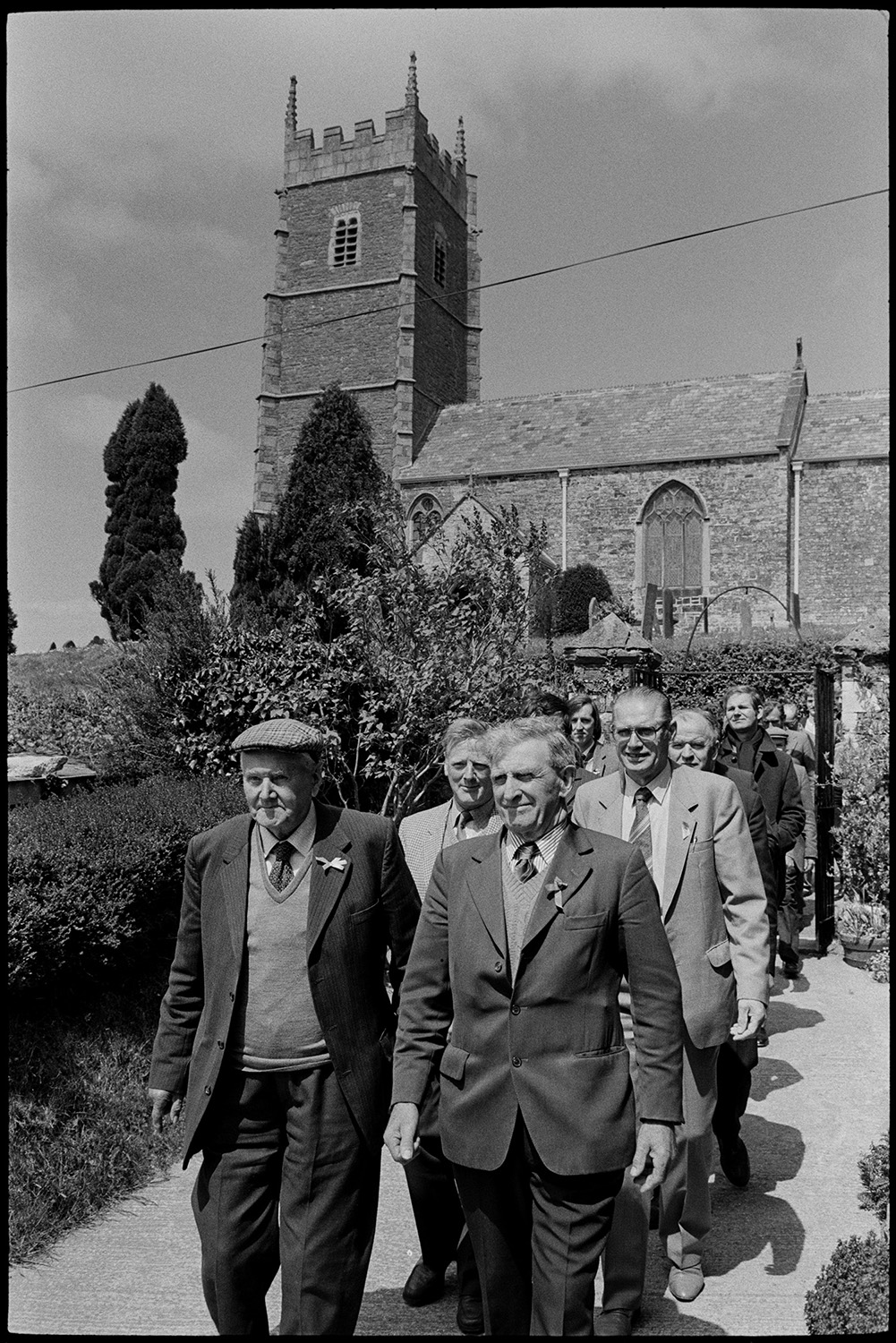 Club Day. Women and club members parading down to village hall with mashed potatoes.
[Men parading down the church path in the Iddesleigh Club Day procession. Iddesleigh Church can be seen in the background.]