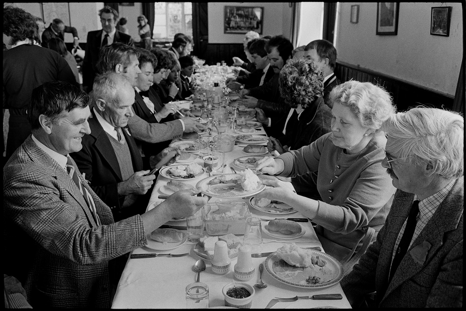 Club Day, standing for grace at club lunch, sitting to eat.
[Men and women sitting on both sides of a long table eating at the Iddesleigh Club Day lunch.]