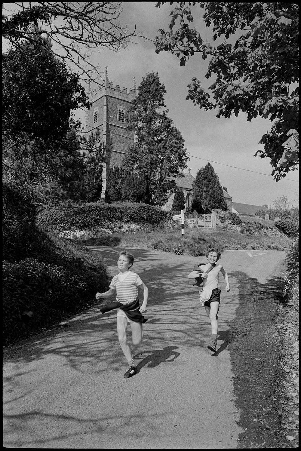 Club Day. Sports, running races, wellie throwing, prizes being given out.
[Two boys running down the road in front of Iddesleigh church on Iddesleigh Club Day.]