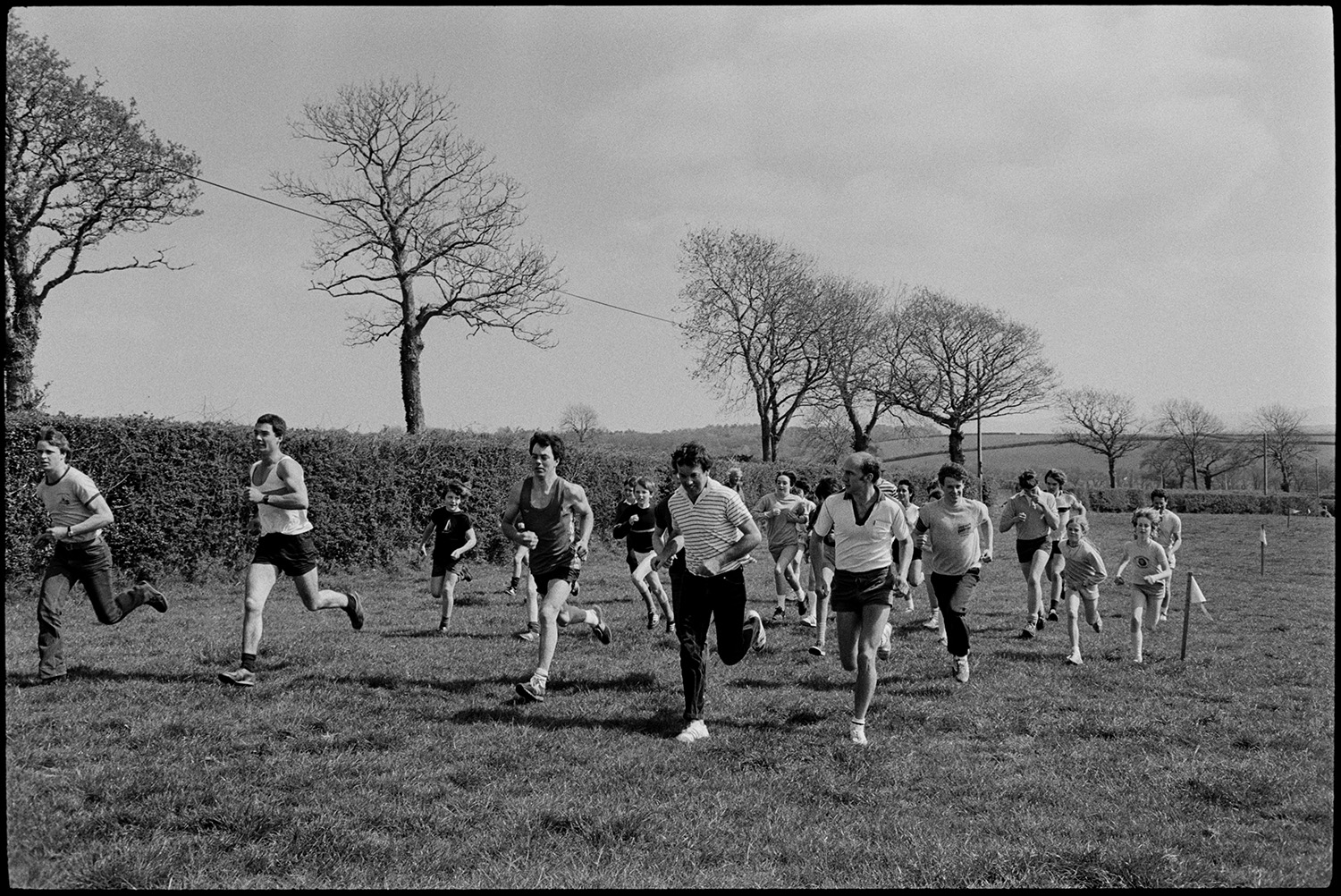 Club Day. Sports, running races, wellie throwing, prizes being given out.
[Runners, including men and children, taking part in a race in a field at Iddesleigh Club Day.]