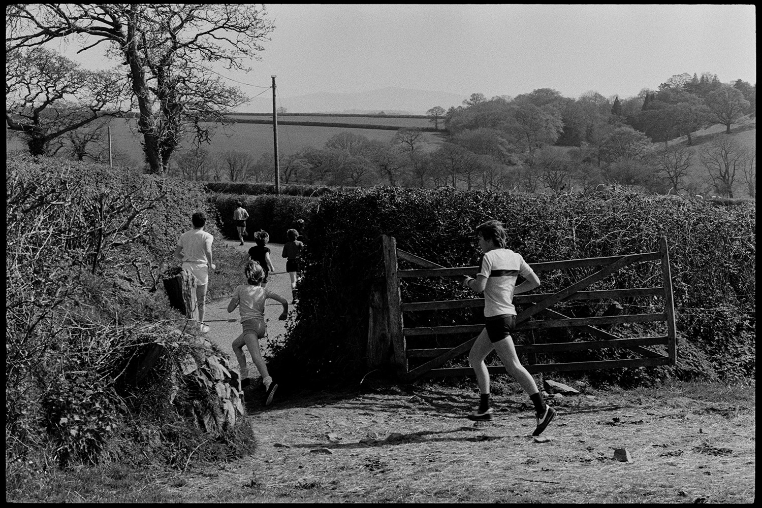 Club Day. Sports, running races, wellie throwing, prizes being given out.
[Men and children running through a field gate and down a road in a race at Iddesleigh Club Day.]