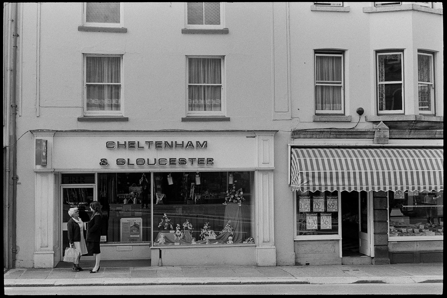 Building Society, Craft Shop, House Agents.
[Two women talking outside the Cheltenham and Gloucester Building Society and a butchers shop in North Tawton.]
